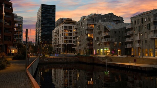 Un quartier urbain situé au bord de l’eau, avec des bâtiments modernes, un canal et un ciel au coucher du soleil.