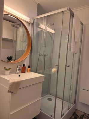 Un bagno moderno con doccia vetrata, uno specchio rotondo, un lavandino bianco e una piccola pianta in vaso.