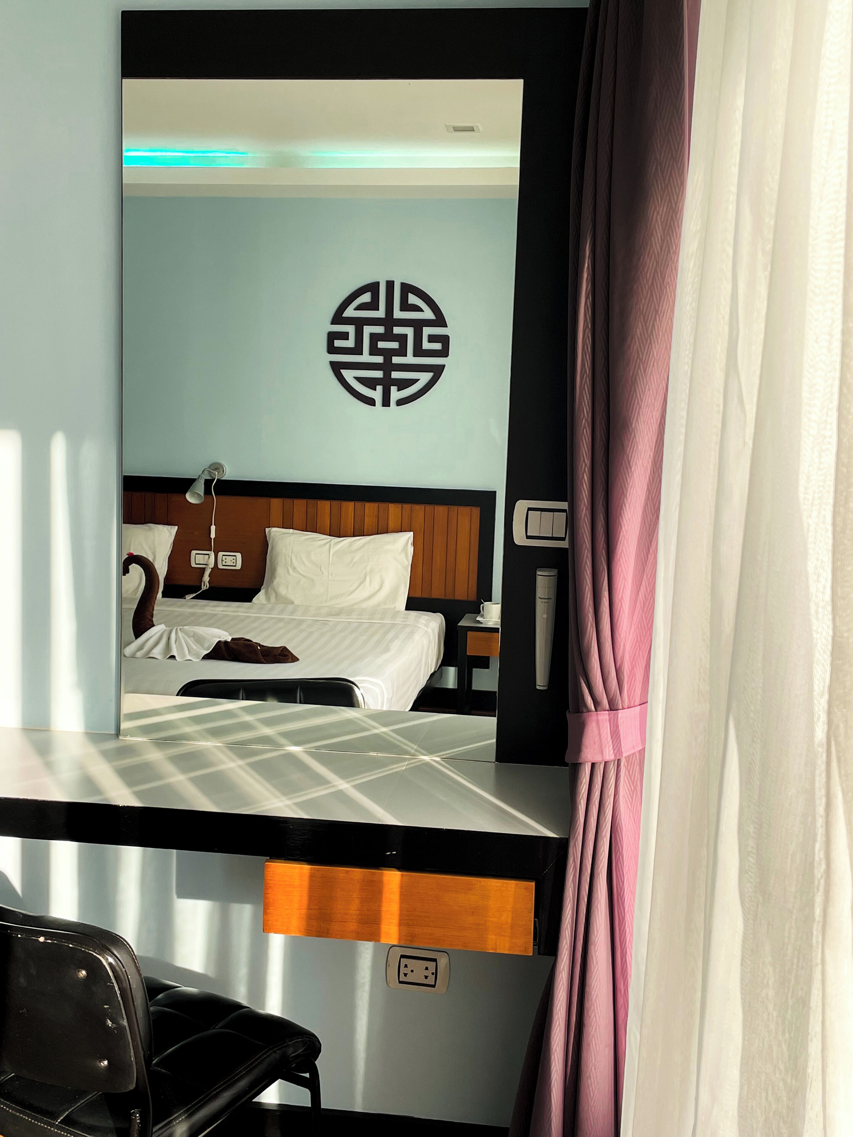 Habitación de hotel con cama, escritorio con silla, espejo, pared con diseño decorativo y cortina.
