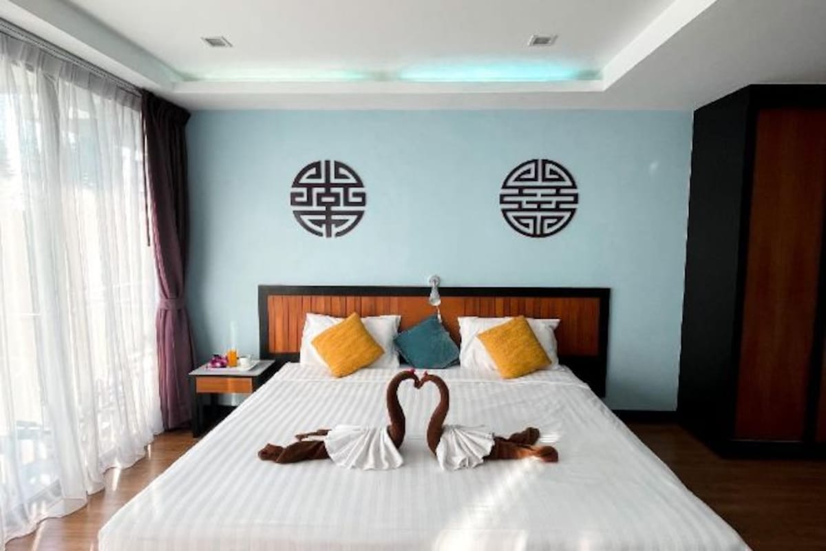 Une chambre d’hôtel avec un grand lit, deux éléments décoratifs sur les murs, une table de chevet et une fenêtre avec des rideaux.