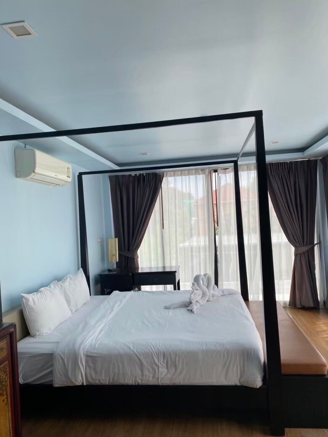 A hotel room with a four-poster bed, a bedside table, a lamp, and a window with curtains.