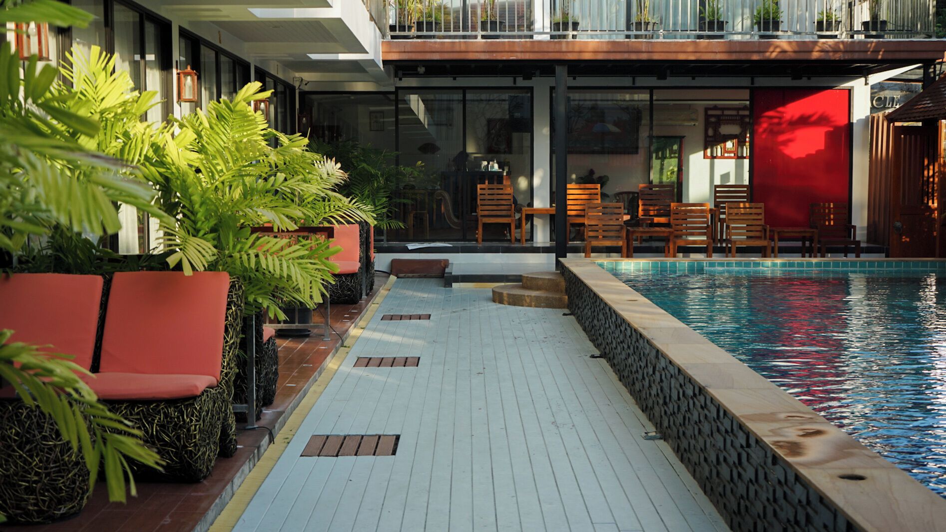 A poolside area with a wooden deck, outdoor seating, and potted plants.