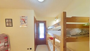 En smal hall med våningssängar på ena sidan och en säng på den andra. På väggen hänger inramade bilder och en affisch.