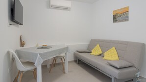 Una sala de estar moderna con un sofá gris, una mesa de comedor con sillas, un televisor de pantalla plana en la pared y un equipo de aire acondicionado.