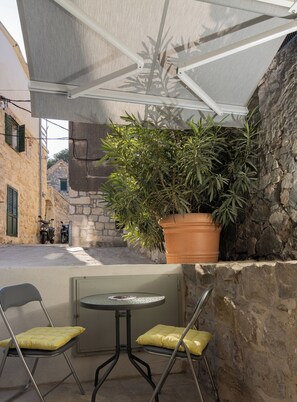 Un petit espace extérieur aménagé avec deux chaises et une table, un pot de fleurs et un mur en pierre.