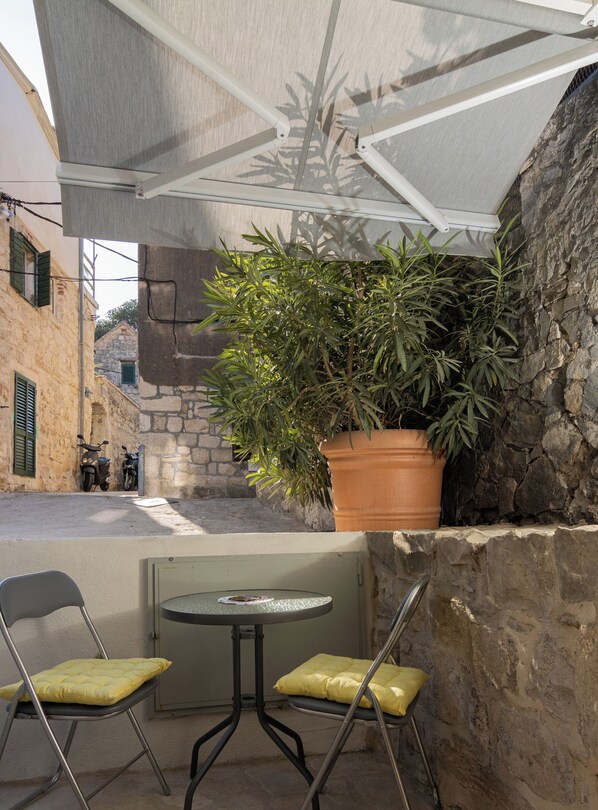Un petit espace extérieur aménagé avec deux chaises et une table, un pot de fleurs et un mur en pierre.