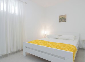 Un lit blanc avec une couvre-lit jaune, une table de chevet blanche et une lampe fixée au mur.