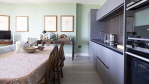 Een moderne keuken met grijze kastjes, een eethoek met een tafelkleed met patroon en ingelijste botanische prints aan de muur.