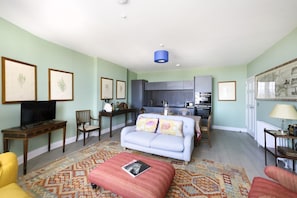 A living room with a sofa, ottoman, and a television. There is a kitchen area with cabinets and a microwave. - Spacious Apartment close to Edinburgh Castle (Edinburgh)