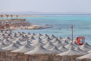 A beach with numerous conical thatched umbrellas and a few wooden structures. - SOULOTEL Emerald Resort & Spa (Marsa Alam)