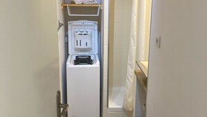 A narrow bathroom with a white washing machine, a shelf with towels, and a shower curtain.