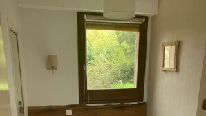 A small, single-bed room with a window providing a view of greenery outside.