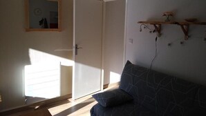 A room with a closed door, a wall-mounted clock, a dark patterned sofa, and a wooden shelf with decorative items.