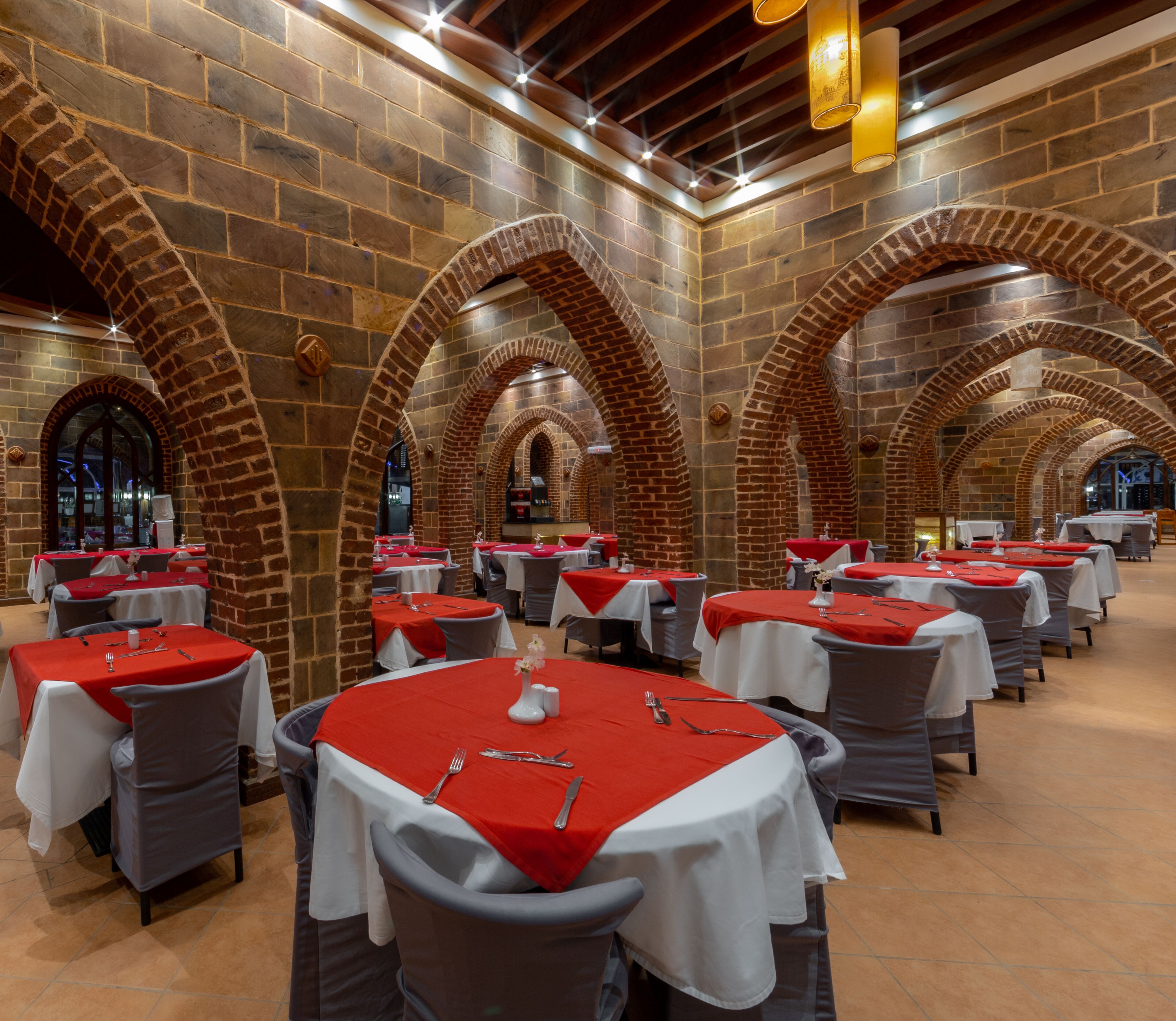 Een restaurant met bakstenen bogen en tafels met rode tafelkleden.