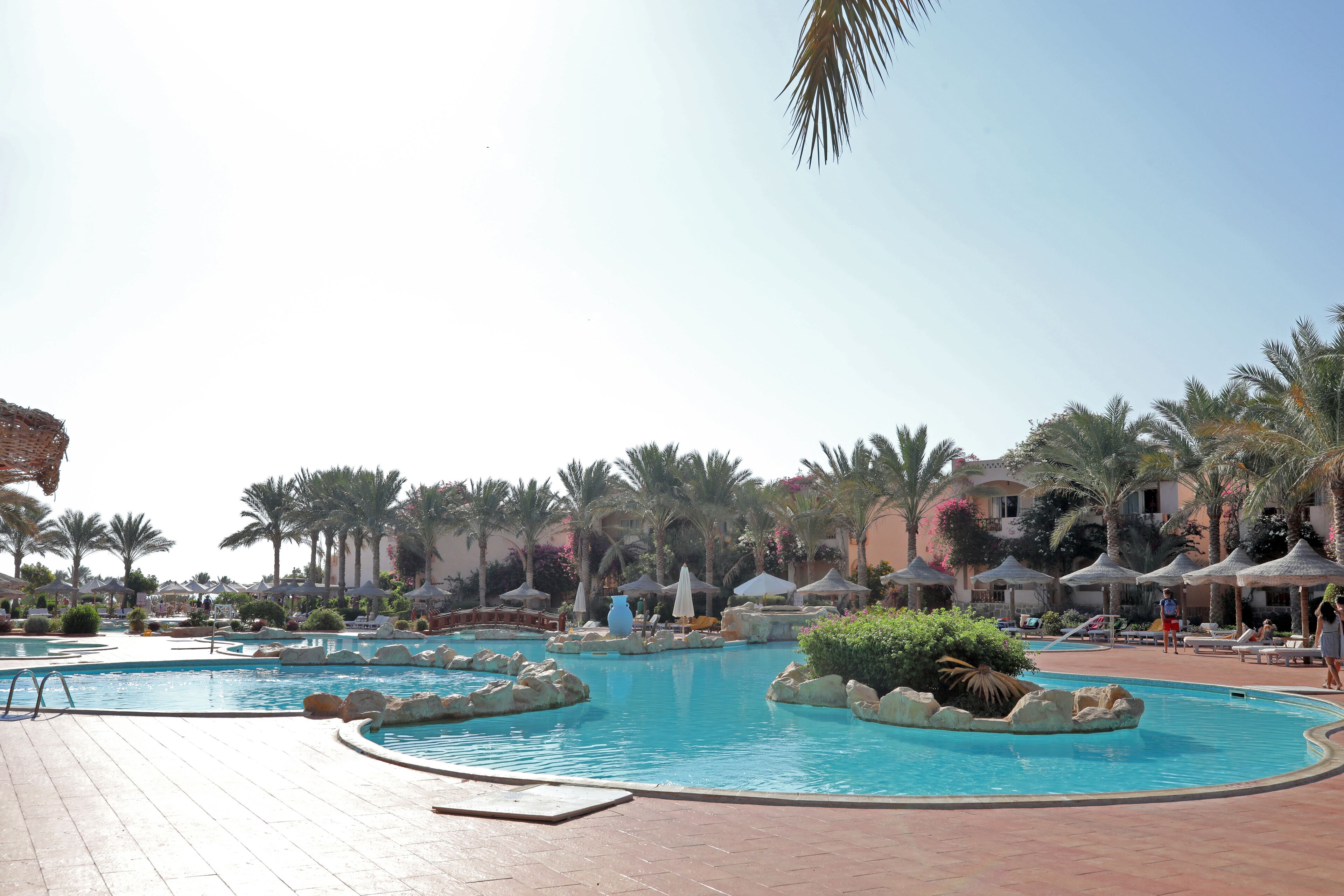 A resort pool area with multiple swimming pools, palm trees, and lounge chairs.
