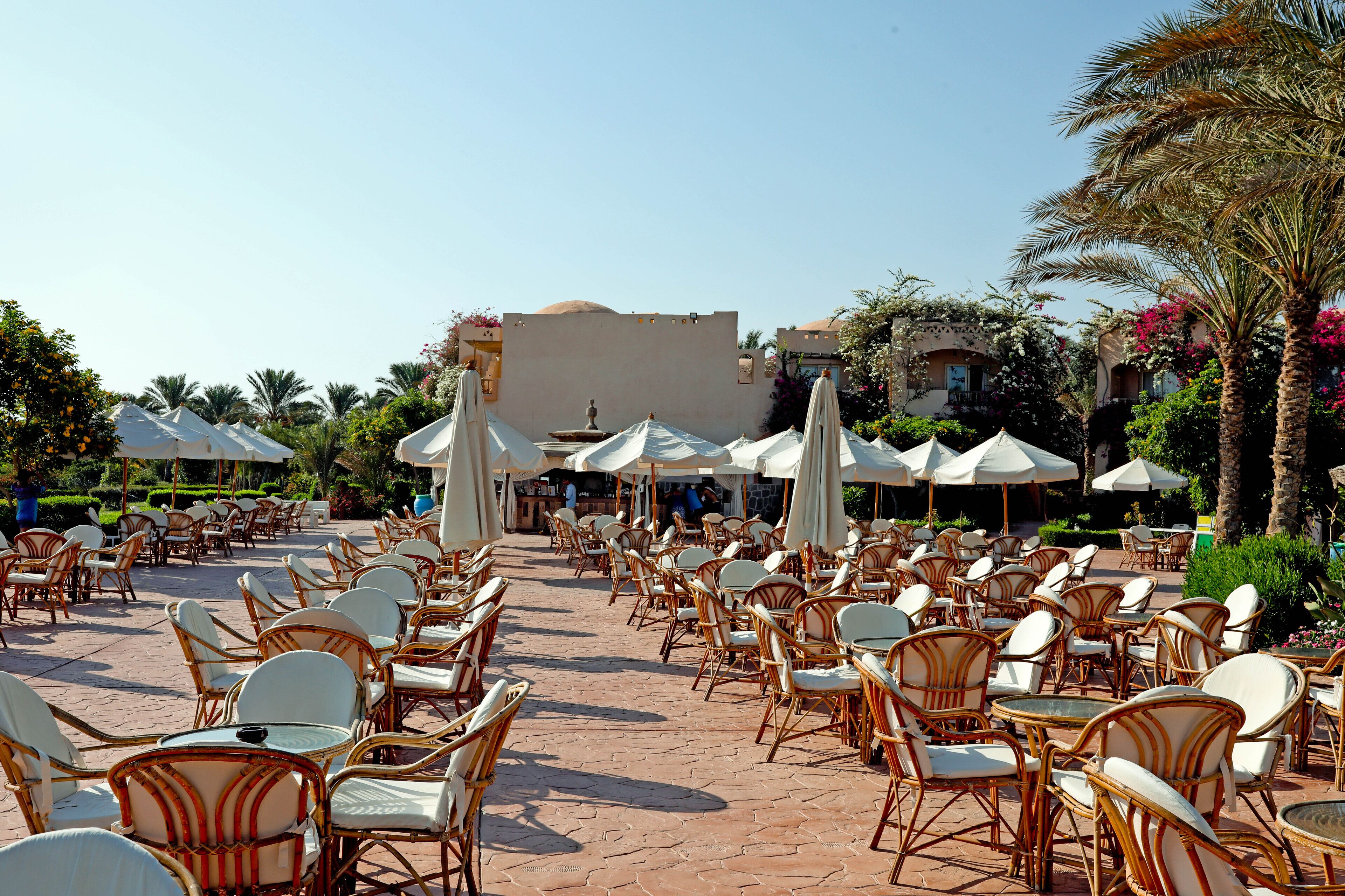 An outdoor cafe area with wicker chairs and tables, umbrellas, and a clear sky.