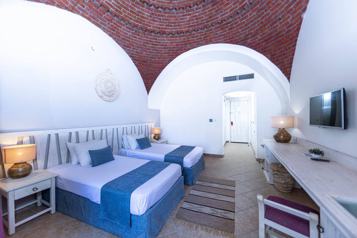 Une chambre d’hôtel avec deux lits, un bureau, une télévision et un plafond en briques.
