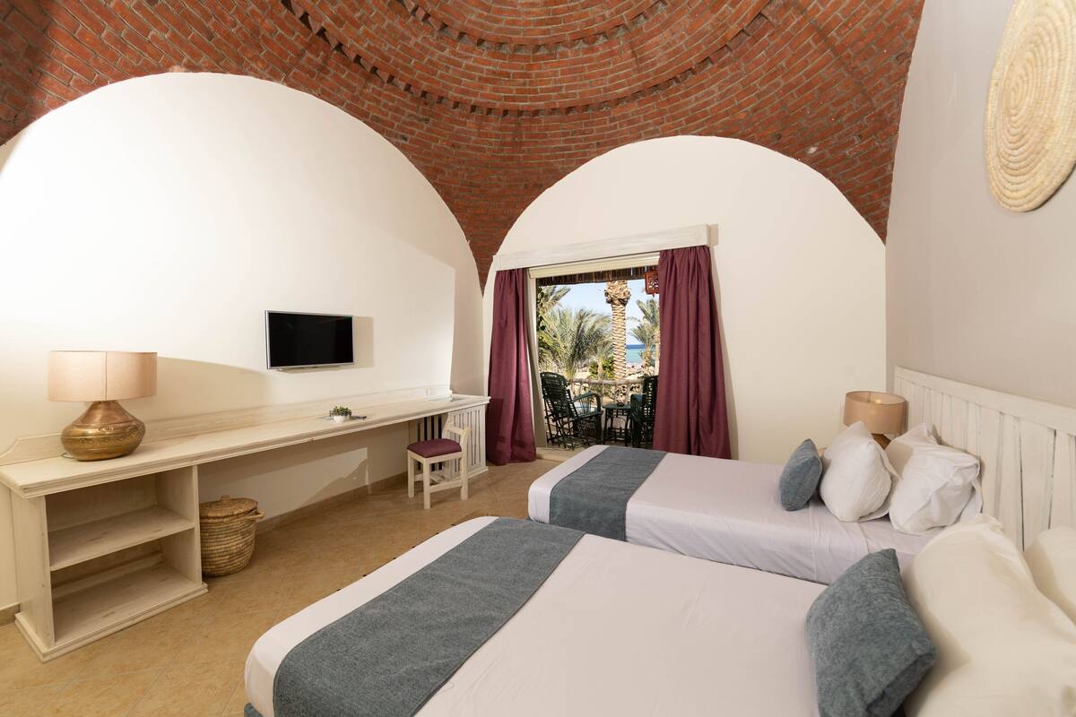 Une chambre avec deux lits, un bureau, une télévision et une vue sur l’extérieur.