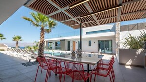A modern outdoor dining area with a glass table and red chairs, overlooking a pool and a mountain view. - Glamorous Villa with Two Swimming Pools and great view (Chania)