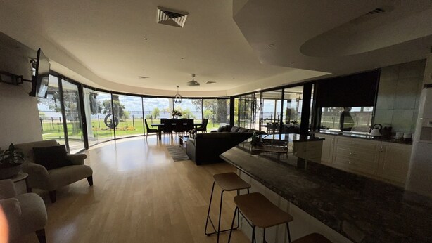 A spacious living area with a curved ceiling, a dining set, and a kitchen with a large window. - Luxury resort style living on Lake Mulwala with breathtaking views & pool/sauna! (Yarrawonga)