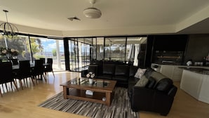 A modern living room with a black leather sofa, a glass coffee table, and a dining area with black chairs. - Luxury resort style living on Lake Mulwala with breathtaking views & pool/sauna! (Yarrawonga)