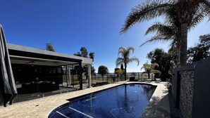 A modern outdoor pool area with a curved design, surrounded by palm trees and a covered seating area. - Luxury resort style living on Lake Mulwala with breathtaking views & pool/sauna! (Yarrawonga)