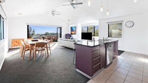 Una cocina moderna con una isla central, una zona de comedor con mesa y sillas, y un amplio ventanal que ofrece vistas al exterior.