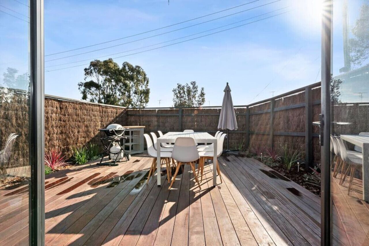 Eine Holzterrasse mit Tisch und Stühlen, umgeben von einem Holzzaun und Pflanzen.