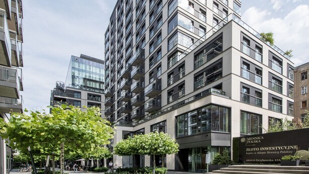 Un immeuble moderne de grande hauteur, doté de nombreux balcons et de grandes fen êtres, entouré de verdure et surplombant un ciel dégagé.