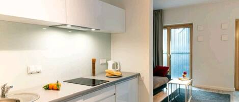 Cocina moderna con armarios blancos, un lavamanos y un ventanal. Hay una pequeña mesa con una taza y un libro. La habitación tiene un ventanal y vistas al exterior.