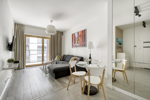 Un salon moderne comprenant un canapé, une table à manger avec des chaises, un téléviseur et une grande fenêtre avec des rideaux.