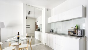 Une cuisine moderne avec des meubles blancs, une table à manger en verre et une machine à café.