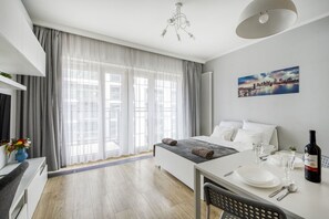 Une chambre d’hôtel moderne comprenant un lit, une table à manger avec des chaises, une fenêtre avec des rideaux, un radiateur et un tableau au mur.