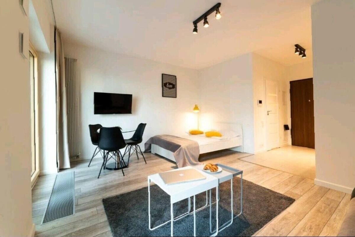 A modern hotel room with a bed, a desk, a chair, a TV, and a small table with a laptop and a plate of food.