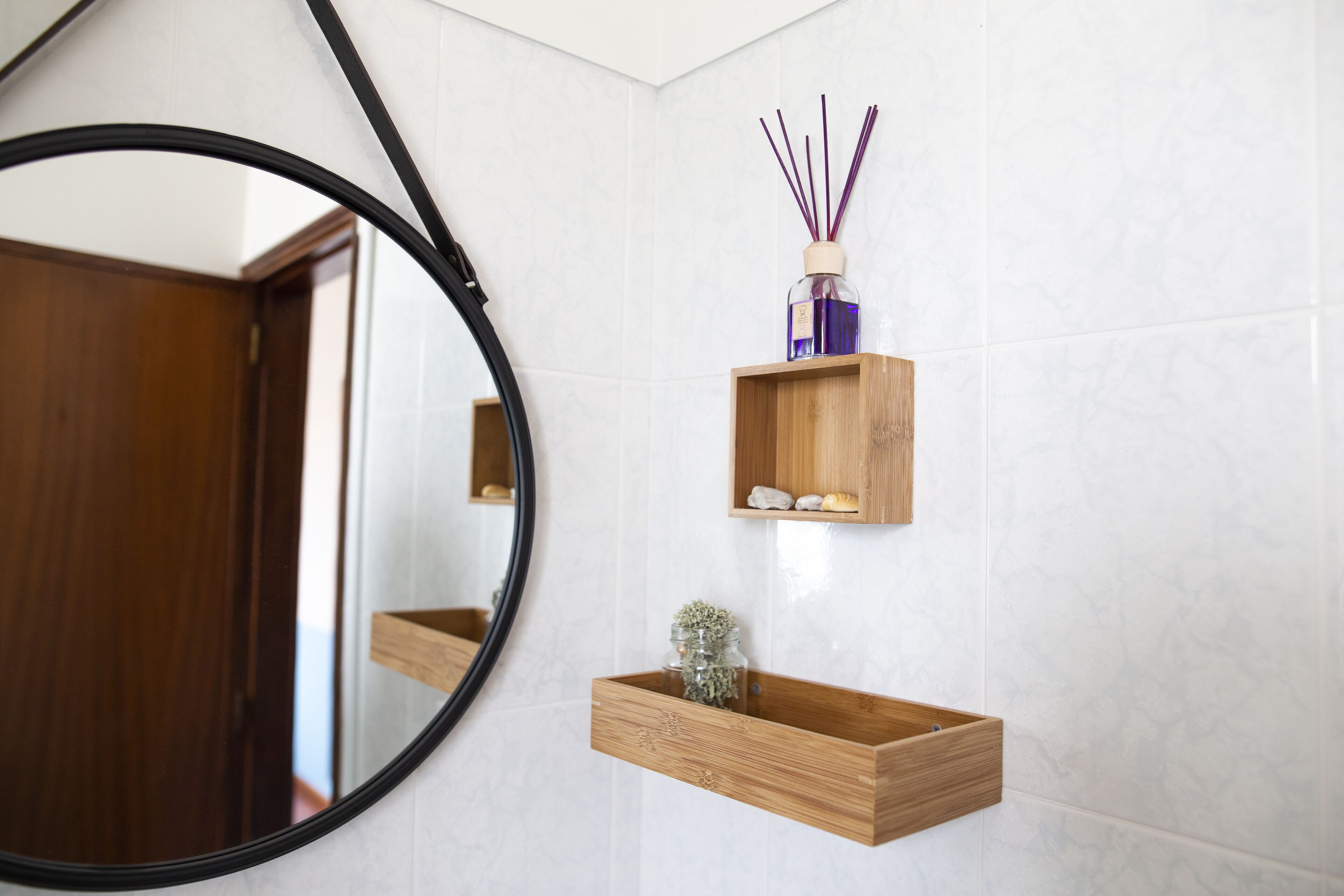 Une salle de bain avec une étagère en bois sur laquelle sont posés un bocal en verre et un flacon de diffuseur à bâtonnets.
