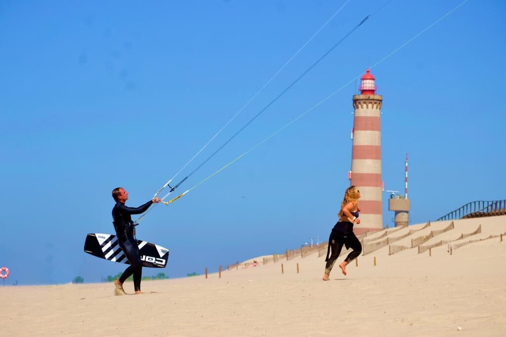Uma praia de areia com um farol ao fundo.