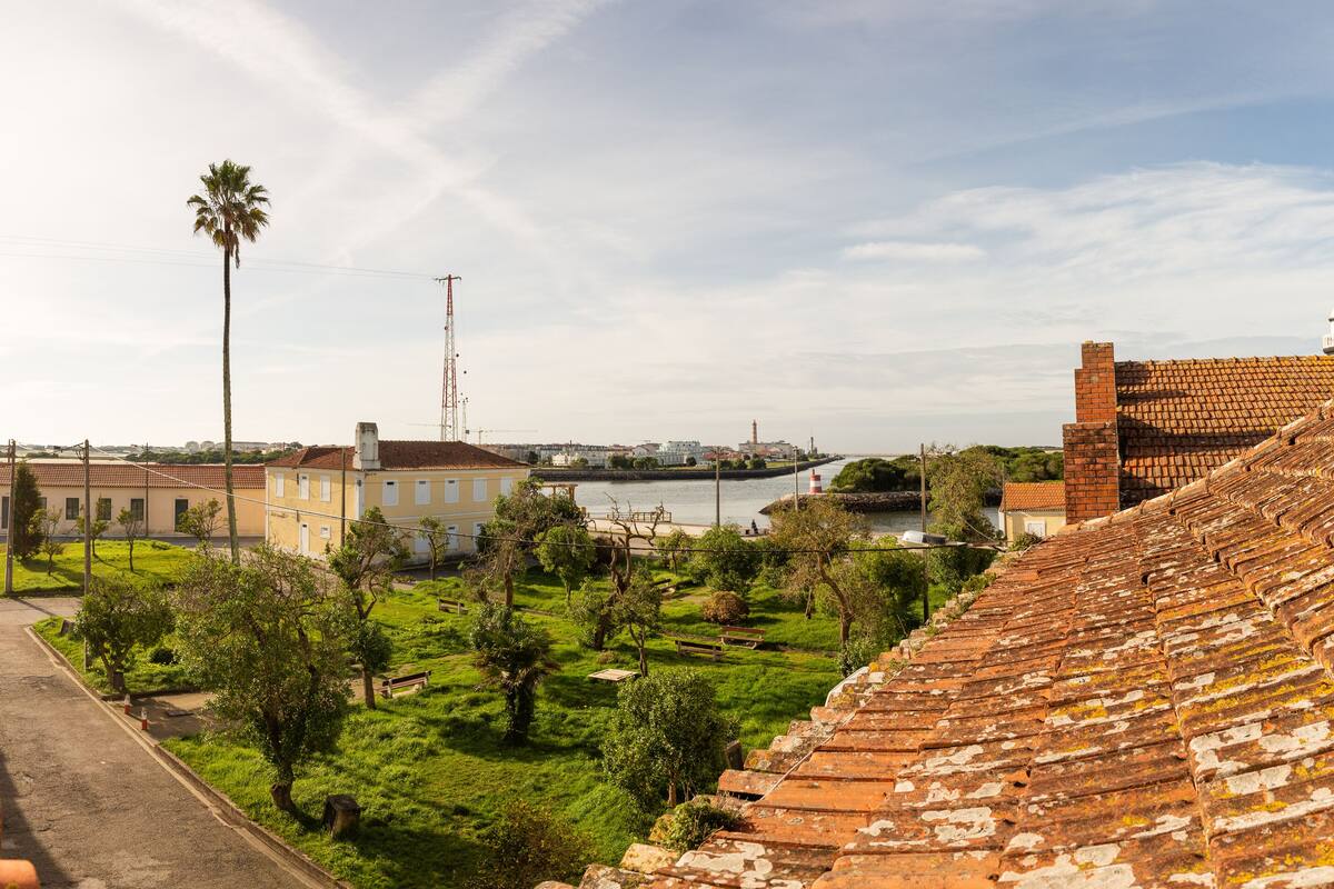 A view of a courtyard with a tiled roof, a palm tree, and buildings in the background.