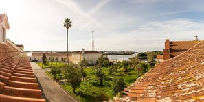 A view of a courtyard with a tiled roof, a palm tree, and buildings in the background. - My Way Kite & Surf House (Ilhavo)
