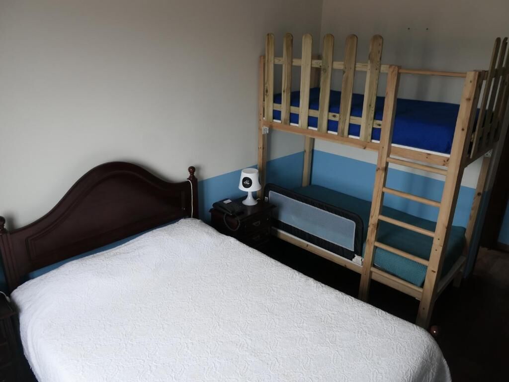 Ein Stockbett mit Holzrahmen und blauer Matratze, ein Holz-Kopfteil und ein kleiner Nachttisch mit Lampe und Taschentuchbox.