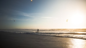 Ein Strand mit einer Person, die Windsurfen geht, dem Meer und einem klaren Himmel.