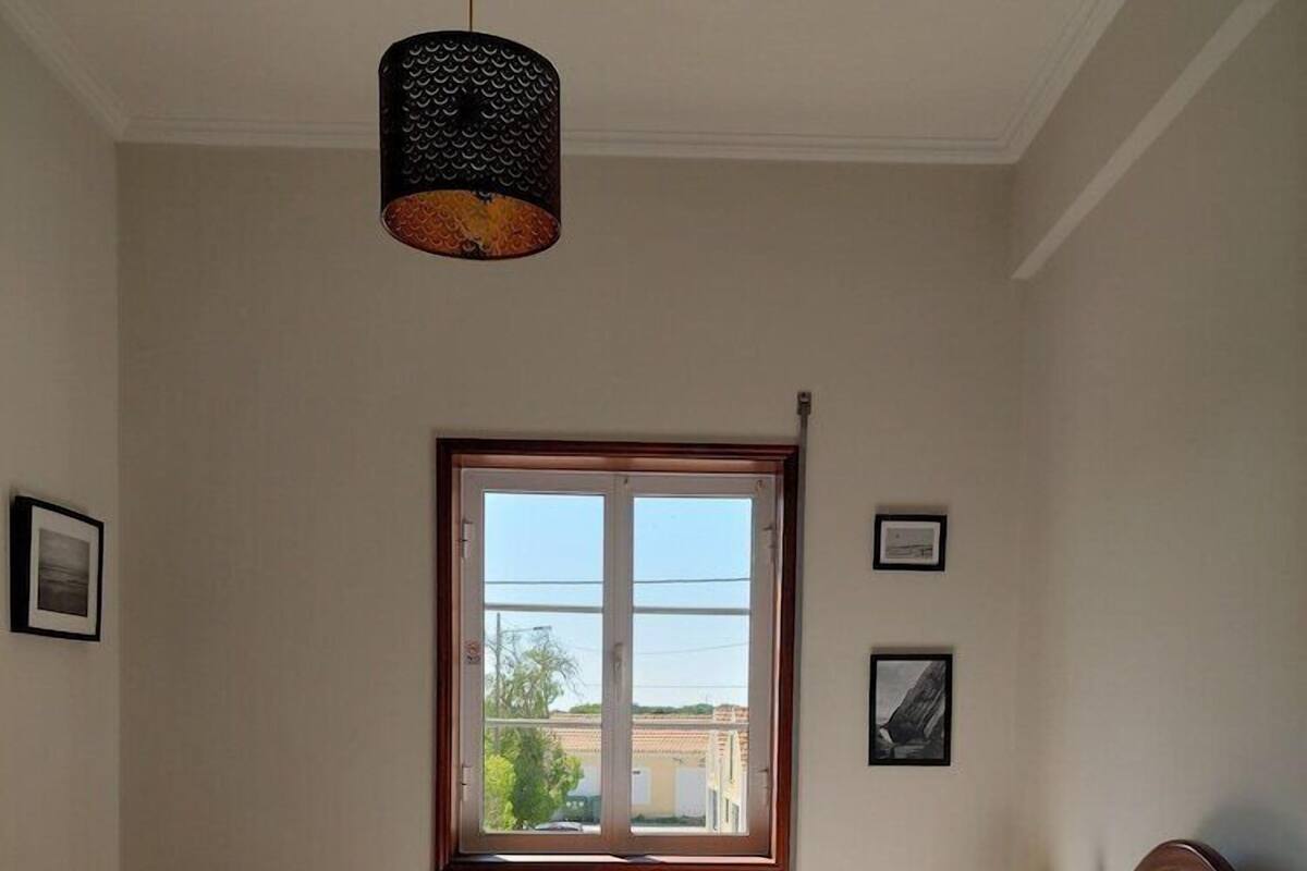 A bedroom with a bed, a window, a radiator, and a hanging lamp.