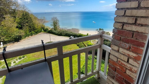 Ein Balkon mit Blick auf das Meer, eine Rasenfläche und eine Ziegelmauer.