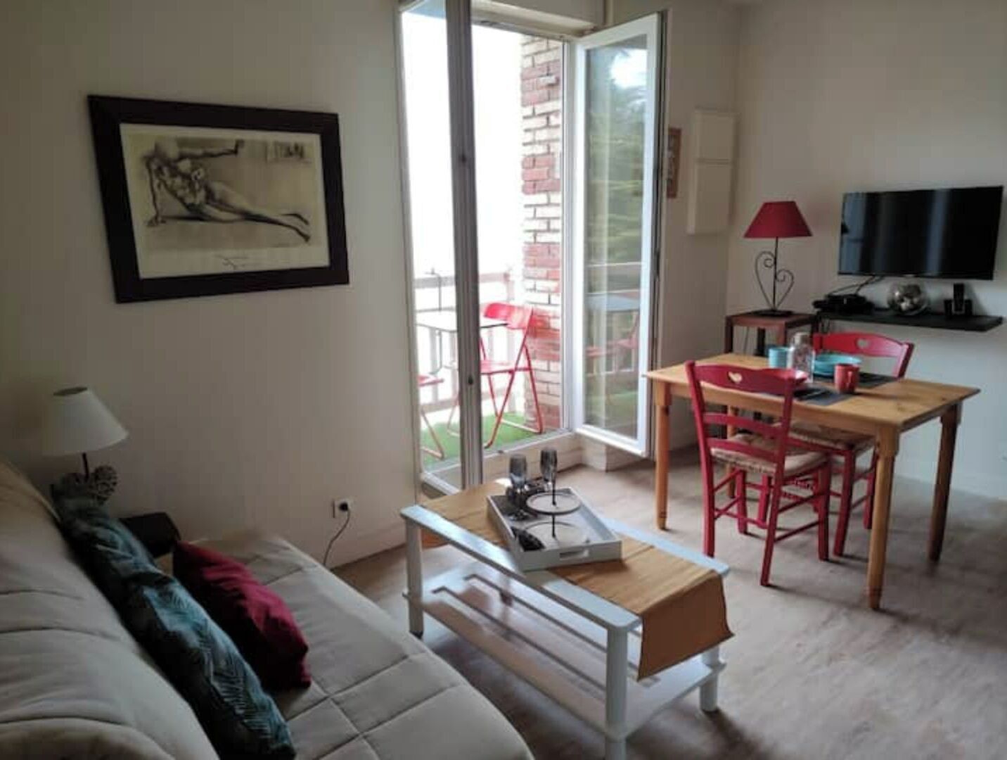 A living room with a sofa, a small table, a TV, and a balcony with chairs.