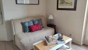 Ein Wohnzimmer mit einem beigefarbenen Sofa, einem Beistelltisch mit Lampe, einer Ablage mit Dekoration und zwei gerahmten Kunstwerken an der Wand.