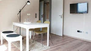 A modern room with a white table, two chairs, a floor lamp, a TV mounted on the wall, and a door leading to another room. - Schiller- Quartier 6 apartment "Heimathafen" (Bremerhaven)