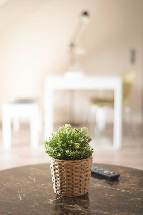 A small potted plant on a round table in a room with a white chair and a lamp in the background.