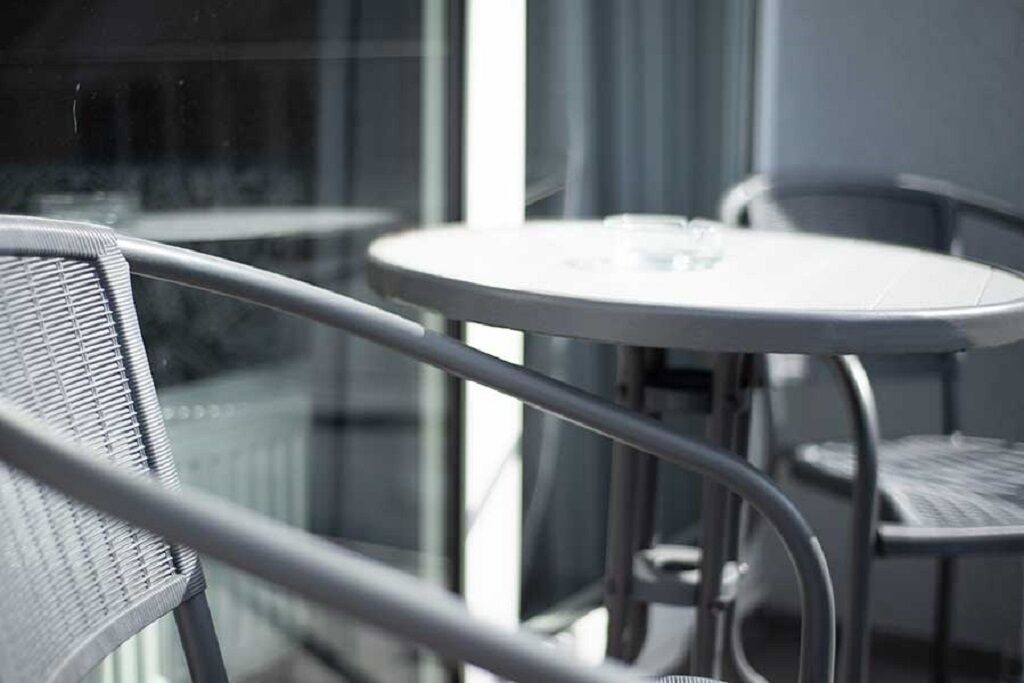 A modern balcony with a round table and two chairs, featuring a clear view of the outside.