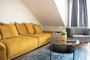 A living room with a yellow sofa, a patterned armchair, a round coffee table, and a small plant.