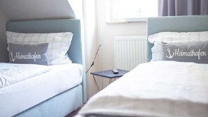A hotel room with two beds, each with a headboard and pillows. There is a small table with a lamp and a remote control. - Schiller- Quartier 6 apartment "Heimathafen" (Bremerhaven)