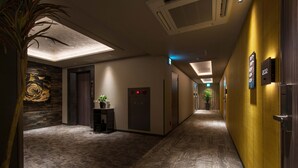 Un couloir d’hôtel au design moderne, agrémenté d’un mur d’accent en bois, d’une plante en pot et d’un ascenseur.